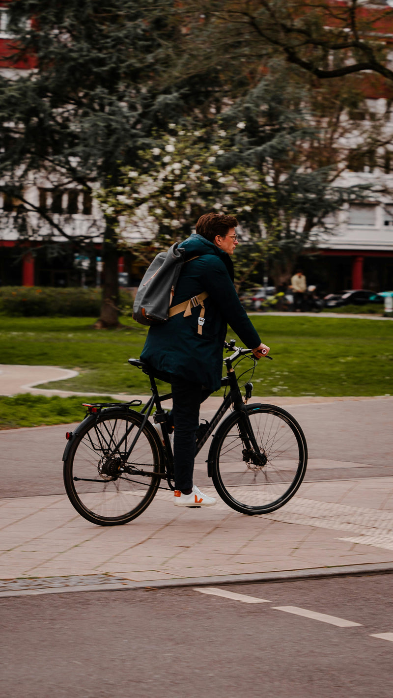 Person riding a bicycle on a sidewalk with trees and buildings in the background