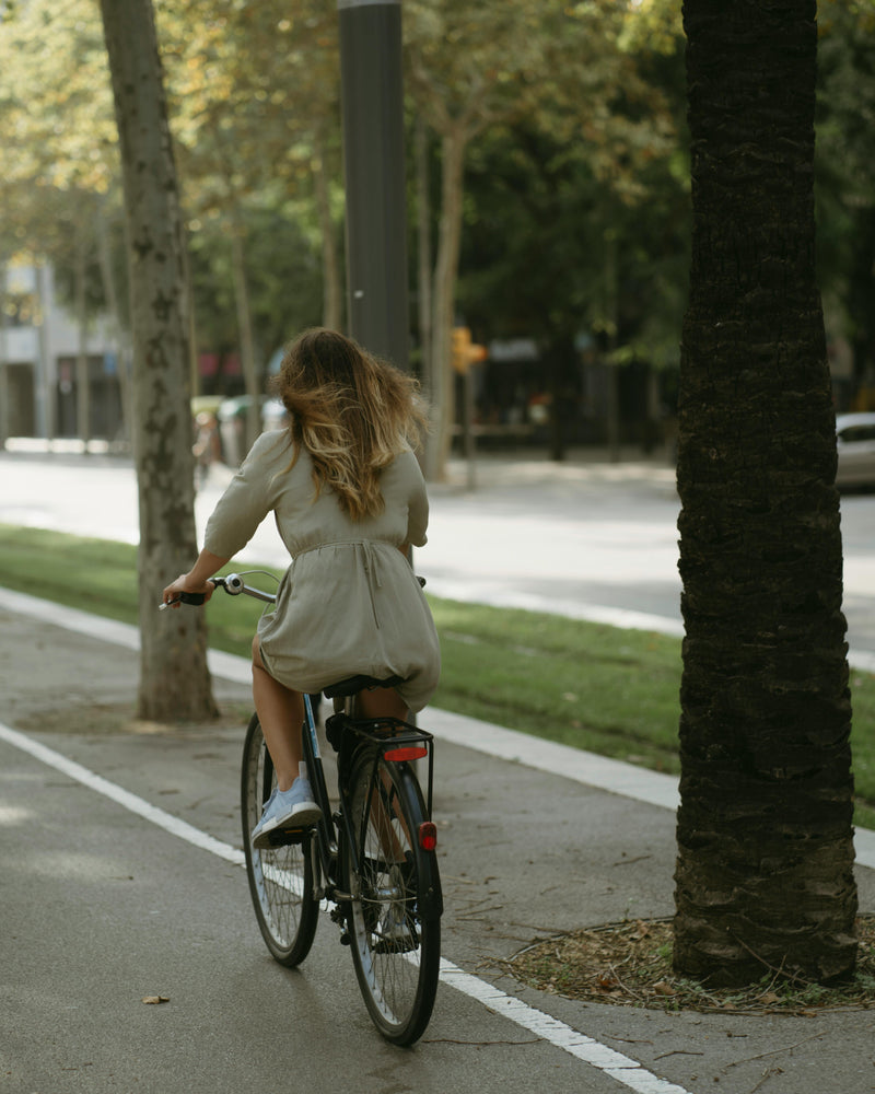 Person riding a bicycle on a sidewalk with trees and a road in the background