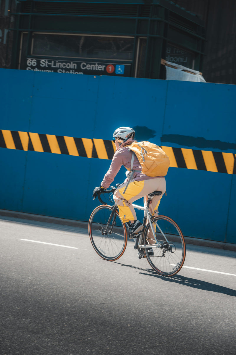 Person riding a bicycle with a yellow backpack on a city street.